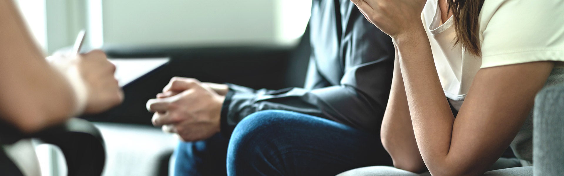 A mediator taking notes while a man and a woman sit on a couch during a divorce discussion.
