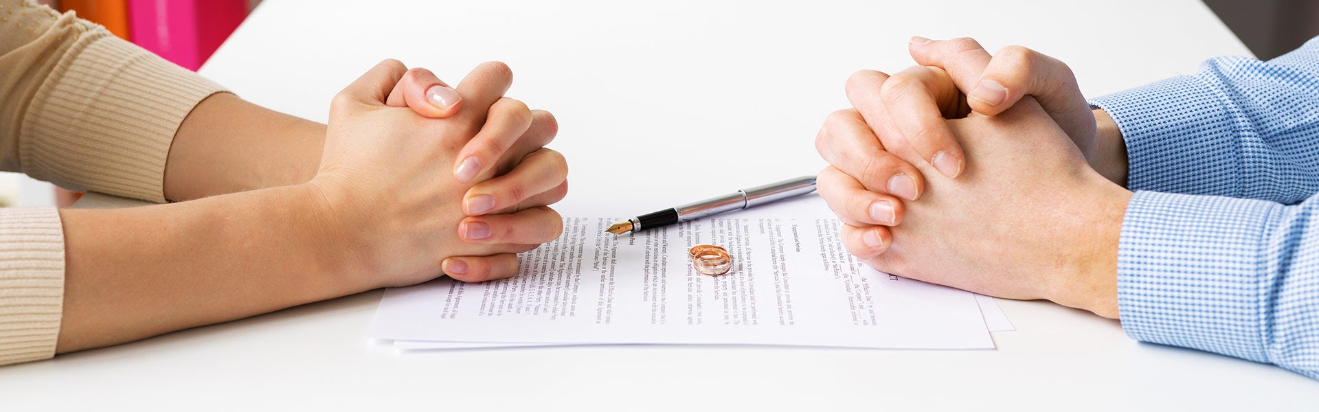 An emotional couple's hands are clasped over divorce papers, symbolizing a difficult breakup.