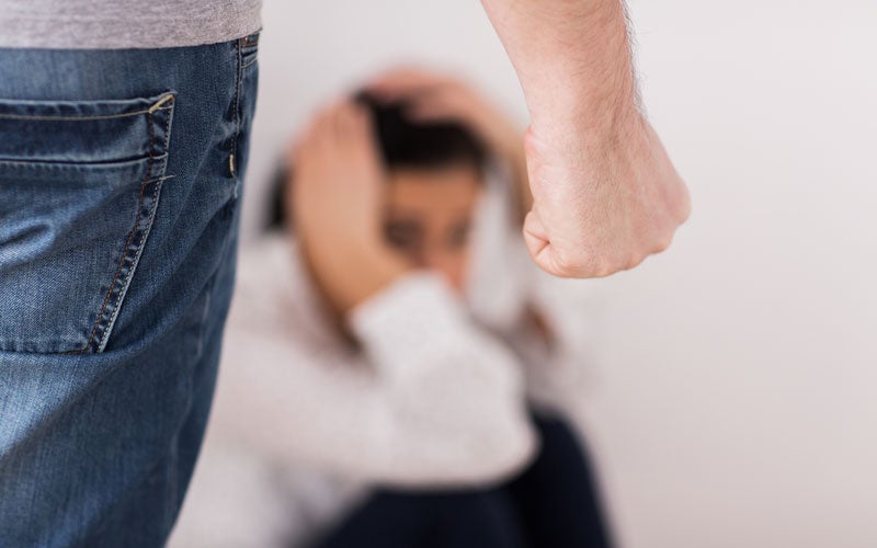 A man’s fist threatens a blurred woman holding her head, symbolizing domestic violence or abuse.