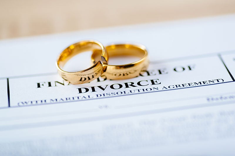Broken gold wedding rings lie atop a divorce document with the word DIVORCE clearly visible.
